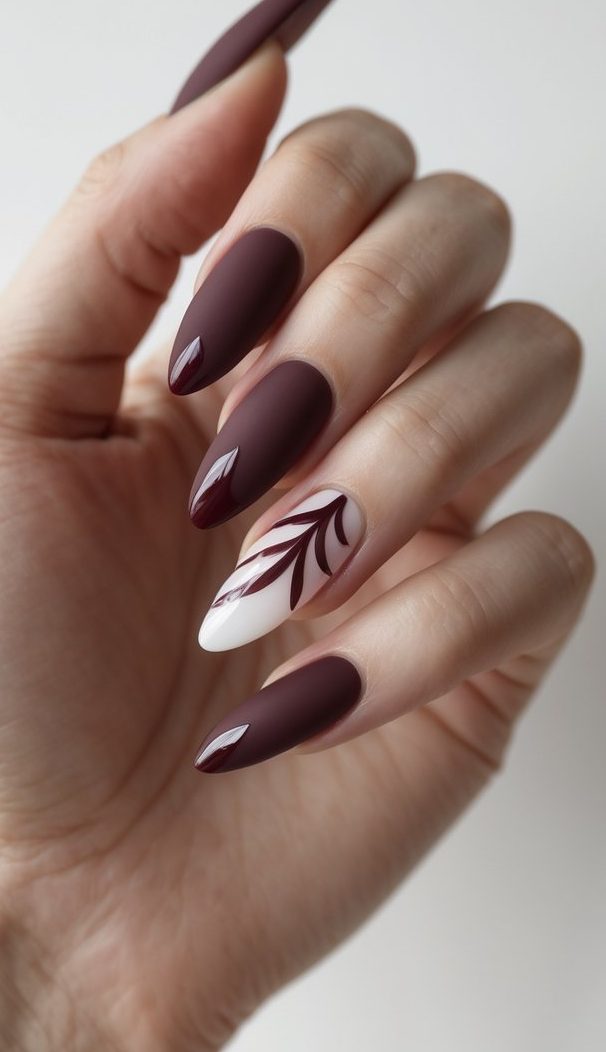 Burgundy long nails with one white nail showcasing a red leaf pattern—an elegant botanical long nail art idea.