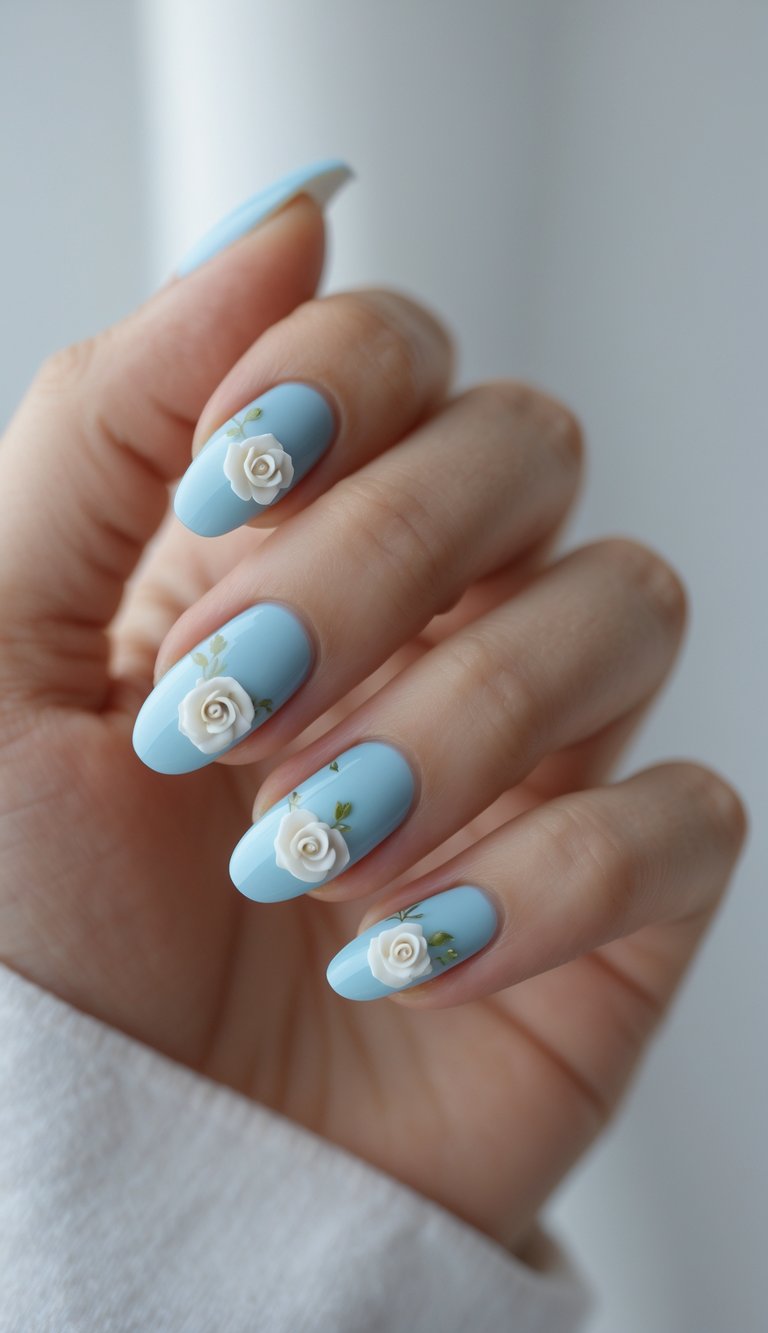 Glossy powder-blue nails on a woman’s hand, each nail decorated with raised white roses and fine green leaf art, creating a dreamy coquette nail art idea.