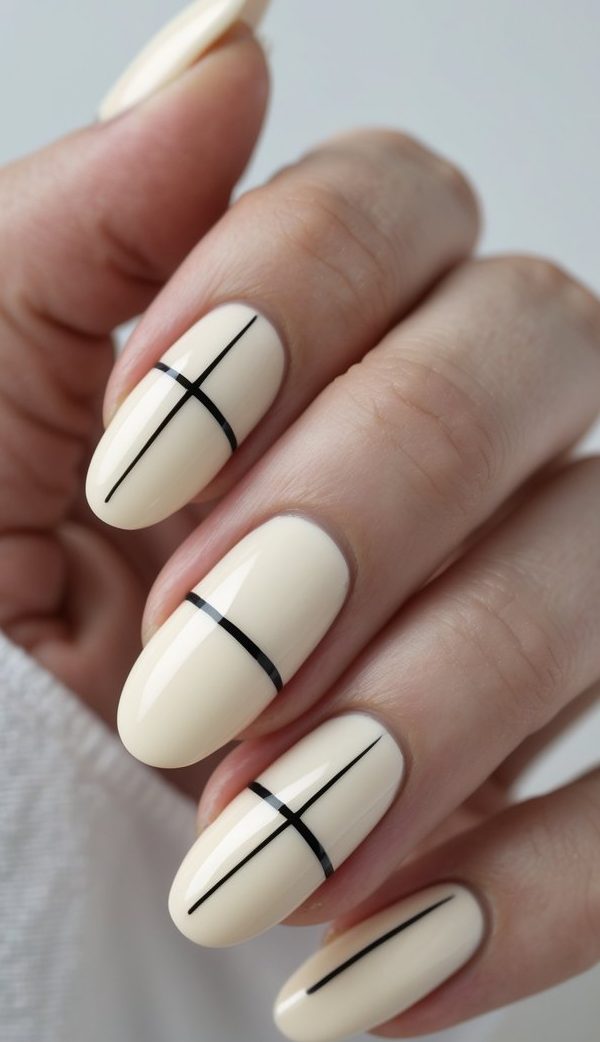 A close-up of neatly painted cream nails, each detailed with fine black striping that mimics ink on paper—a minimalist, artful sophisticated nail art idea.
