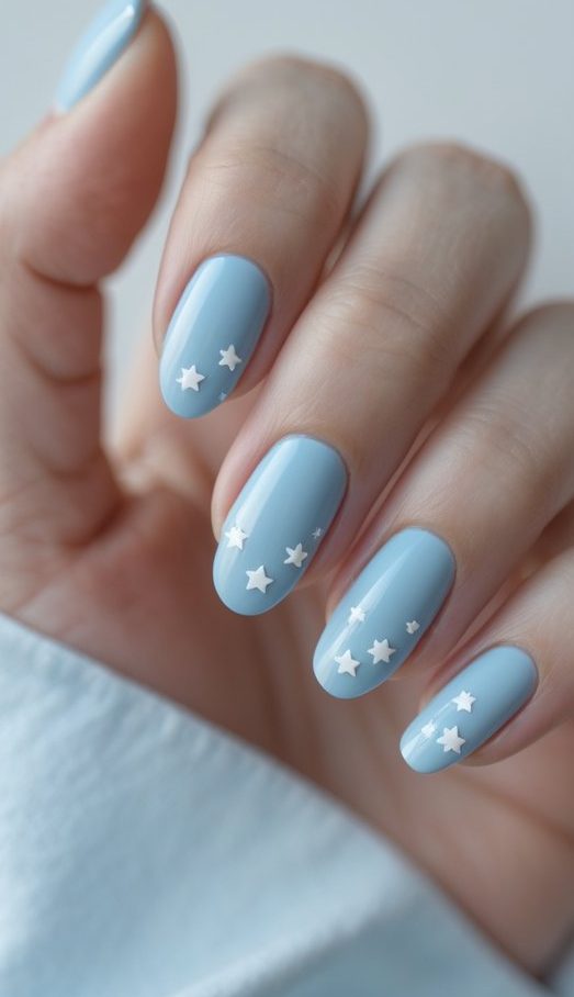 A hand with soft blue nails decorated with scattered white star accents, showcasing a delicate nail art idea with a whimsical night-sky vibe.