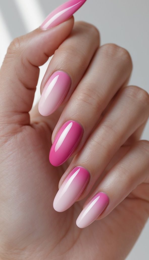 A feminine hand with almond-shaped nails featuring ombre nail art ideas that transition from soft baby pink to bold fuchsia with a glossy finish.