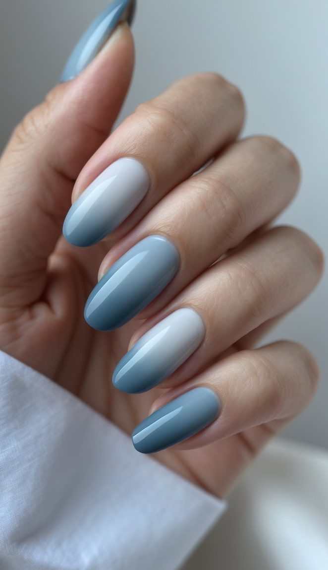 A hand showing ombre nail art ideas with soft blue fading into cool gray on long almond-shaped nails.