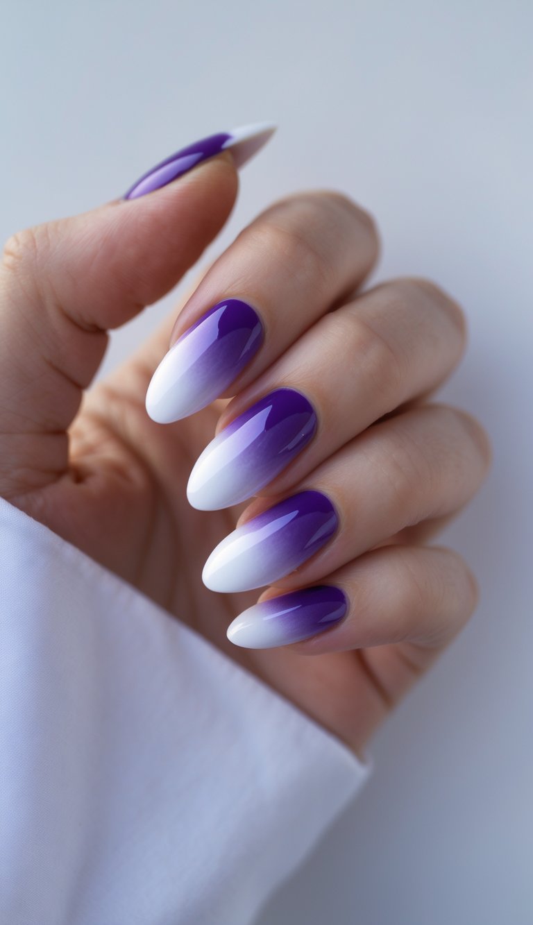 Angled fingers display a purple and white nail art idea using a smooth purple ombré that transitions into white tips on long almond nails.