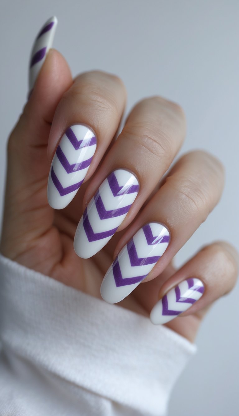 Fingers curled slightly show a purple and white nail art idea with white nails decorated by symmetrical purple chevron patterns under soft lighting.