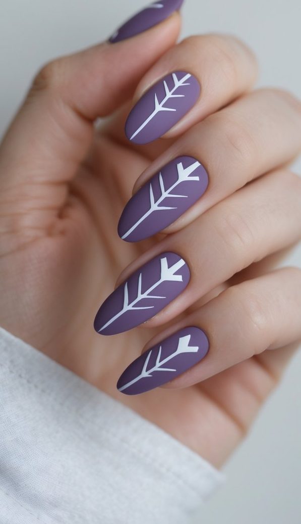 A hand angled toward soft light reveals matte purple nails detailed with white leaf designs, showcasing a modern purple nail art idea with structured, minimal lines.