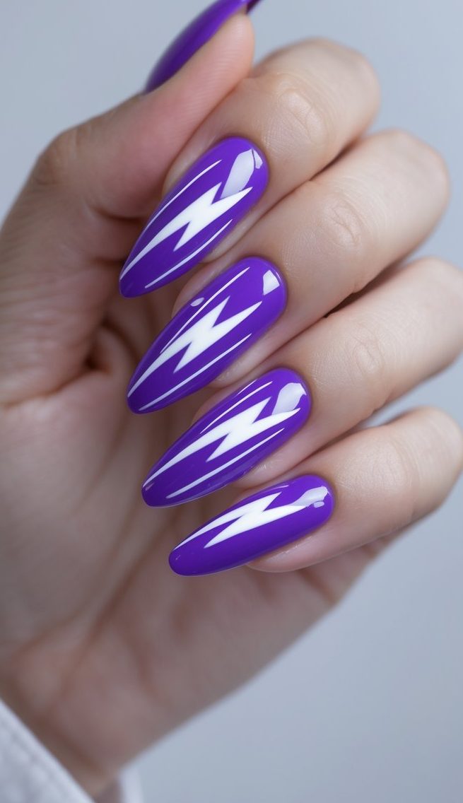 An angled view of a hand reveals shiny purple stiletto nails marked with sharp white lightning designs, presenting a powerful purple nail art idea.
