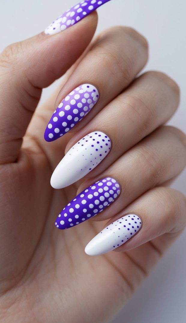 An angled hand shot highlights alternating purple and white almond nails with minimalist polka dot designs, showcasing a balanced purple nail art idea.