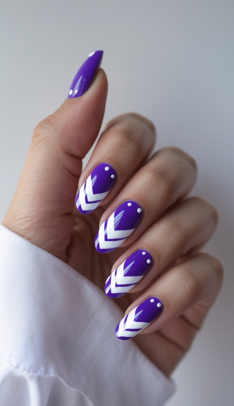 A hand posed against a neutral background shows glossy purple nails with white chevron stripes and tiny dot accents, highlighting a purple nail art idea.