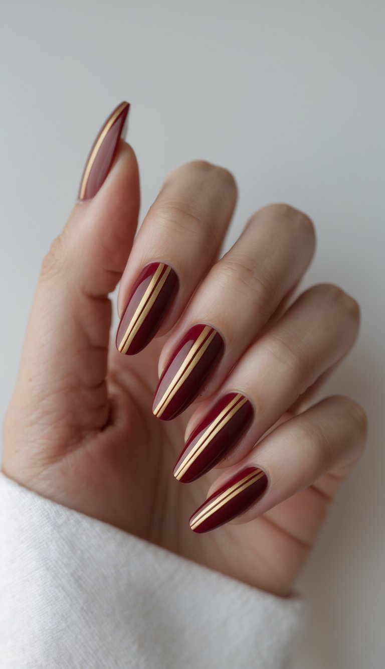 Close-up of a hand with red nails decorated with gold stripes on a white background.