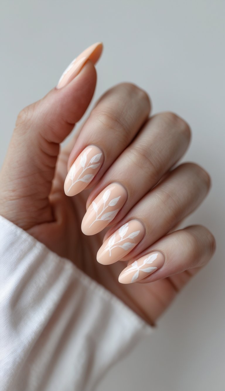 Close-up view of one hand with pale peach nails decorated with delicate leaf designs on a white background.