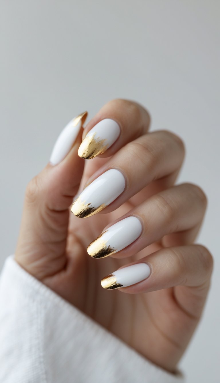 Close-up of one hand with white nails featuring gold foil tips against a white background.