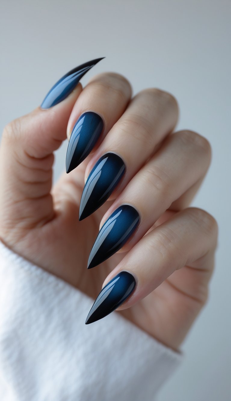 Close-up of one hand with dark blue to black gradient ombre nails with sharp tips against a white background.