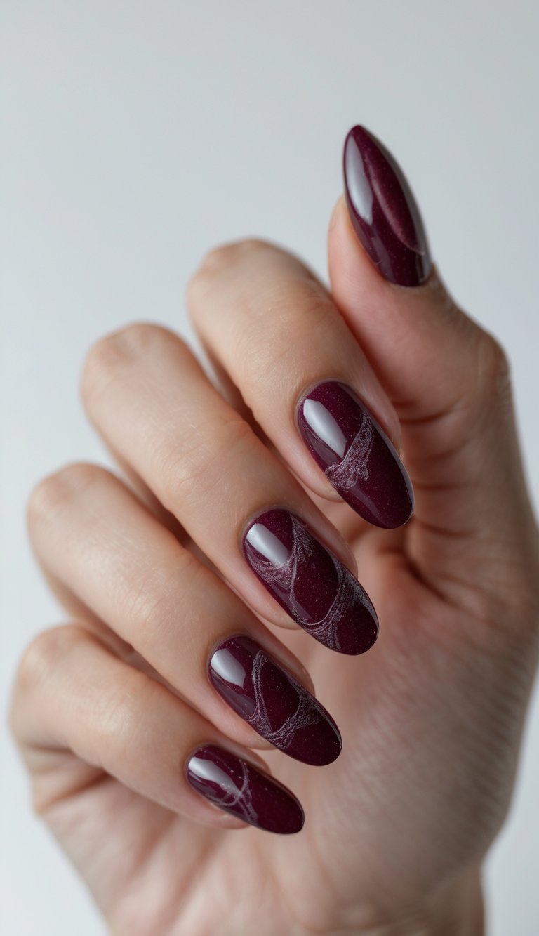 Close-up of a hand with deep cranberry shiny nails featuring detailed nail art against a white background.