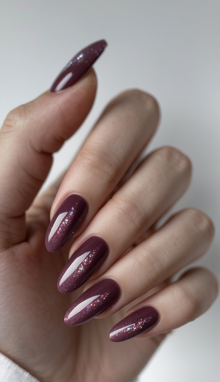 Close-up of one hand with burgundy nails featuring shimmer details against a white background.