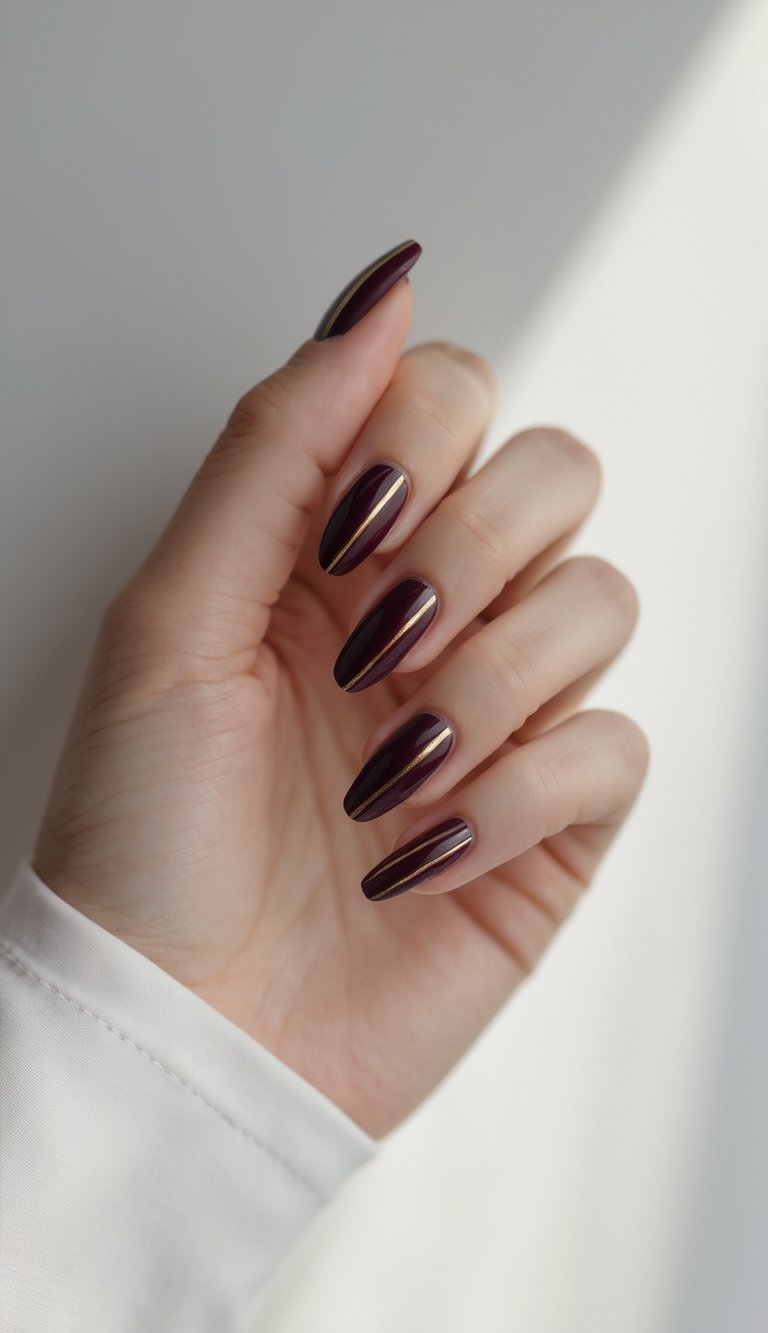 Close-up of one hand with deep wine-colored nails decorated with thin gold stripes against a white background.