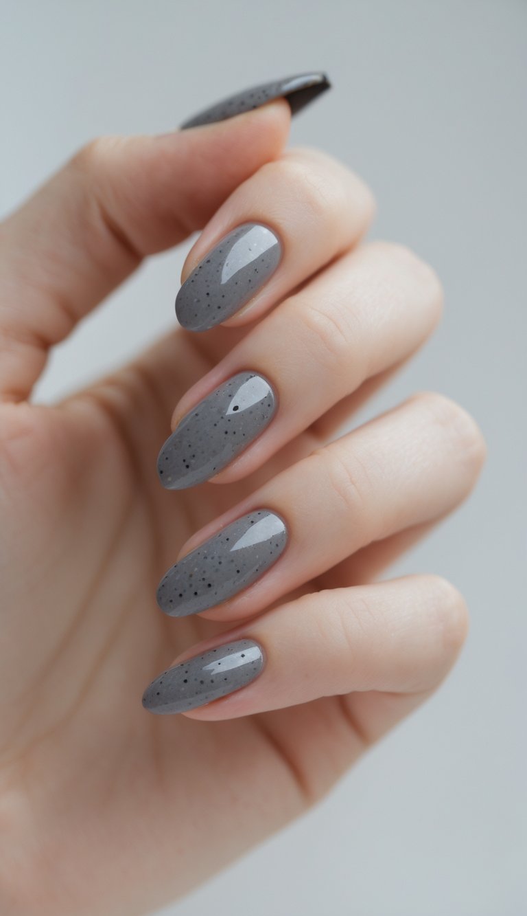 Close-up of one hand with nails painted smoky gray featuring black speckles against a white background.