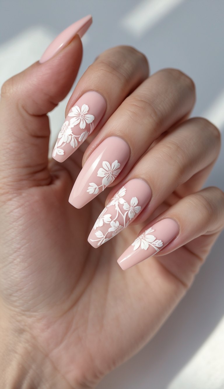 Close-up of one hand showing soft pink ballerina-shaped nails with white floral designs on a white background.