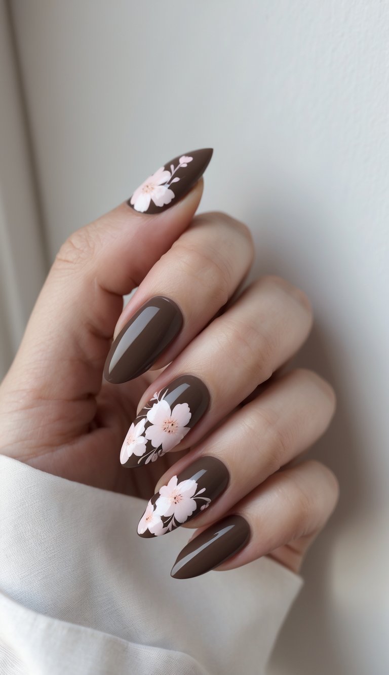 Close-up of a single hand with chocolate brown nails decorated with soft pink floral designs against a white background.