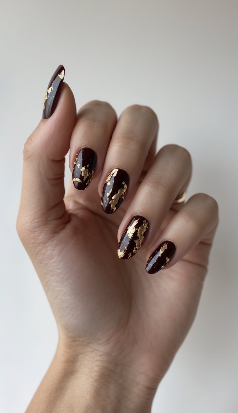 Close-up of one hand with dark red nails decorated with chipped gold flakes against a white background.