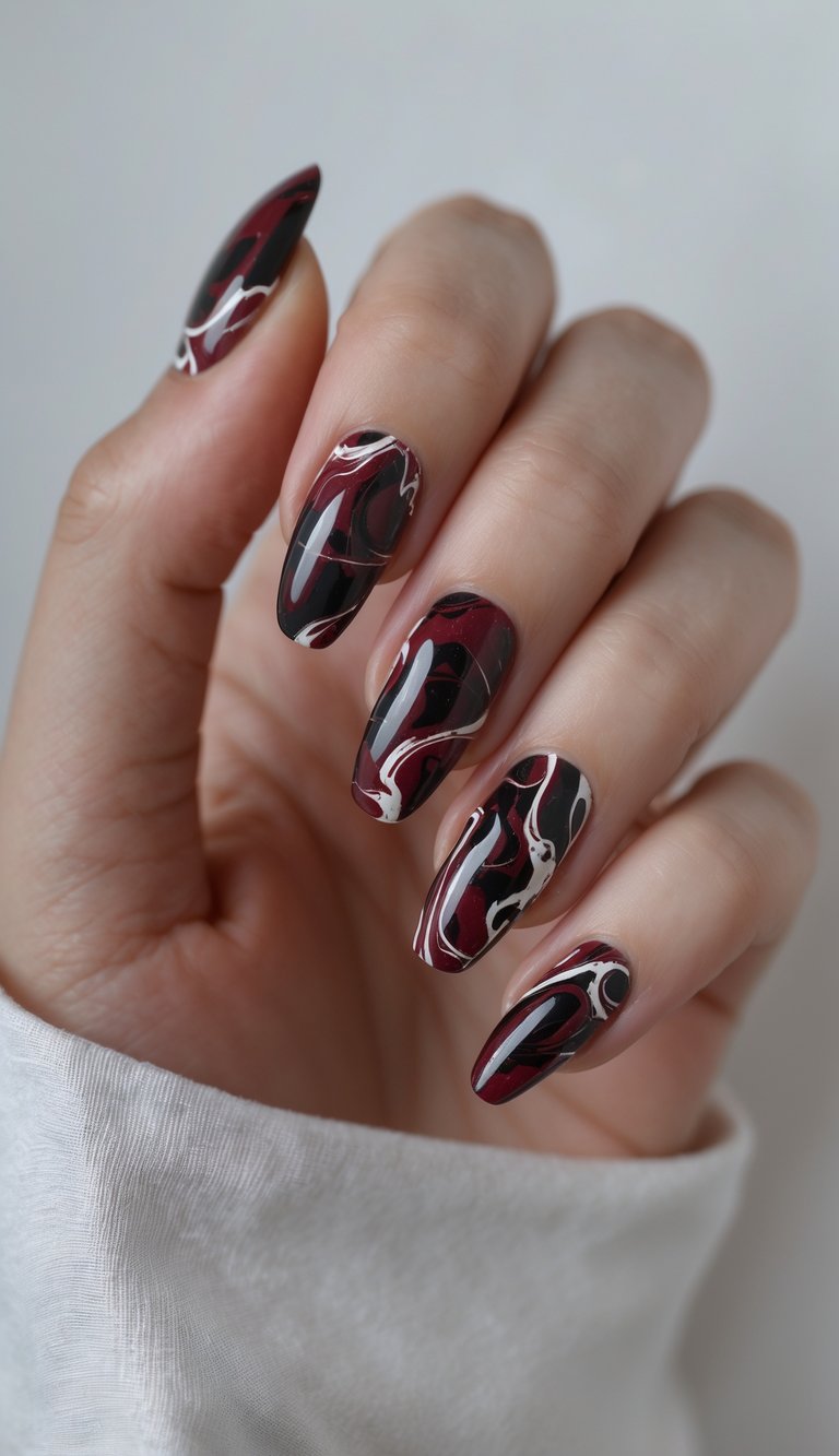 Close-up of one hand with deep crimson marble swirl nail art on a white background.