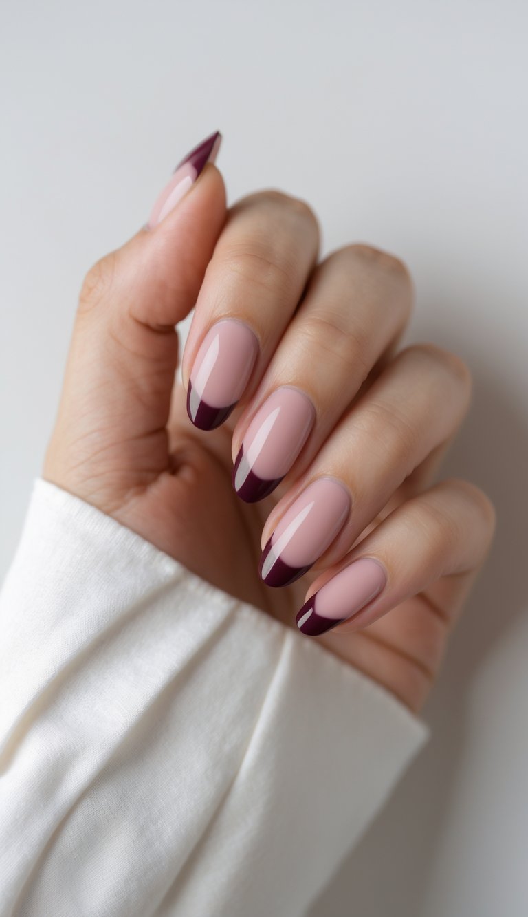 Close-up of one hand showing nails with French tips painted in a deep wine color against a white background.