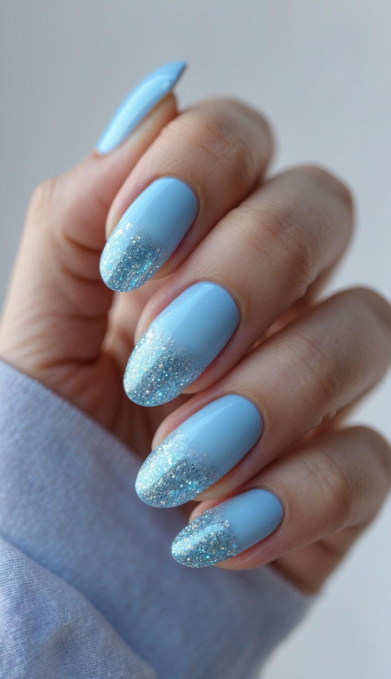 Close-up of one hand with baby blue nails featuring glittery ombre gradient nail art on a white background.