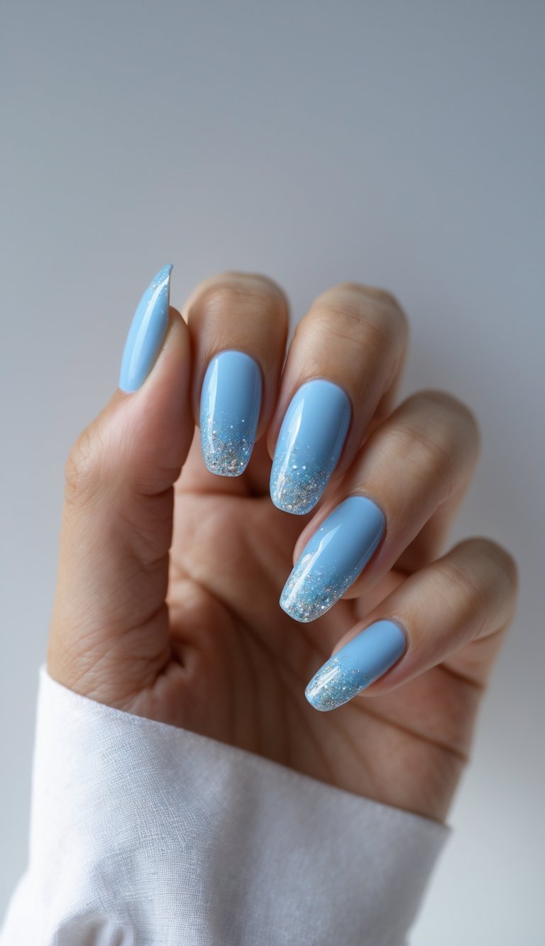 Close-up of one hand with sky blue nails and glitter gradient tips against a white background.