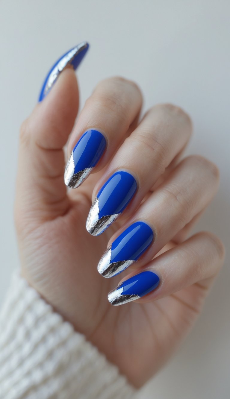Close-up of one hand with royal blue nails featuring silver foil tips against a white background.