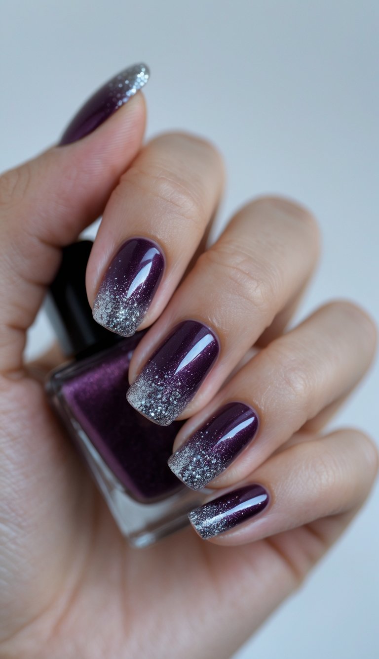 Close-up of one hand showing dark plum nails with glitter ombre nail art against a white background.