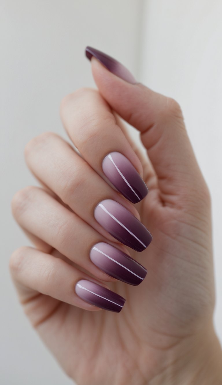 Close-up of one hand with plum ombré nails featuring simple patterns against a white background.
