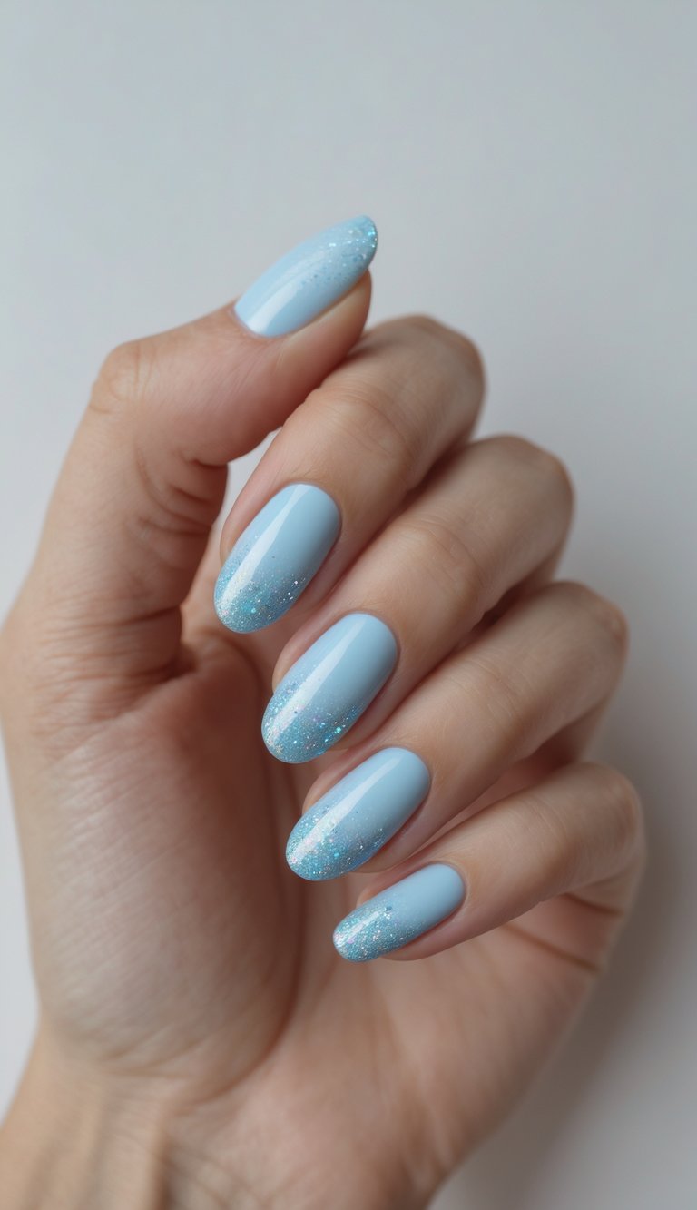 Close-up of a single hand with baby blue nails featuring sparkly ombre nail art against a white background.