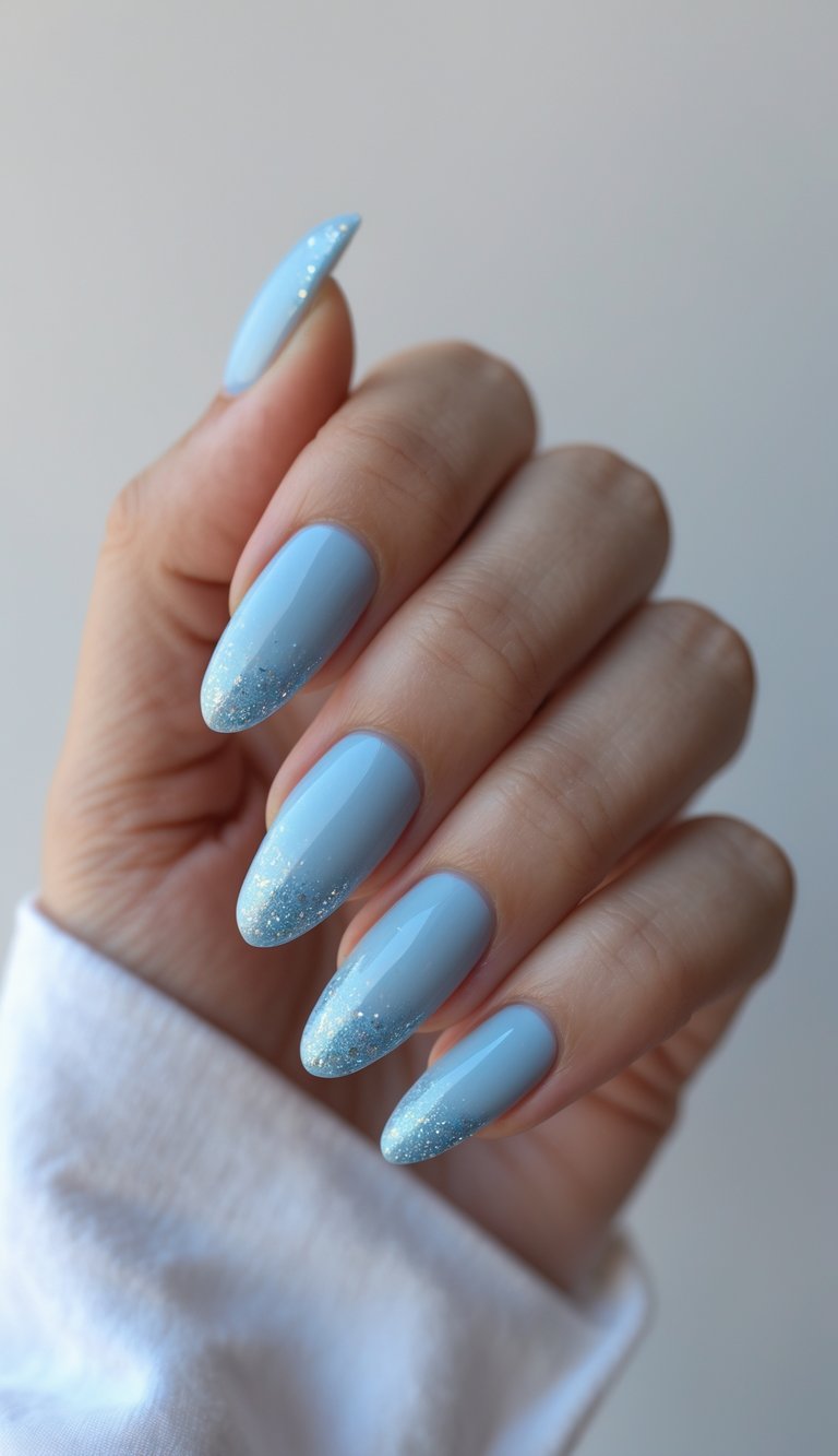 Close-up of one hand with sky blue nails and glittery ombré tips against a white background.