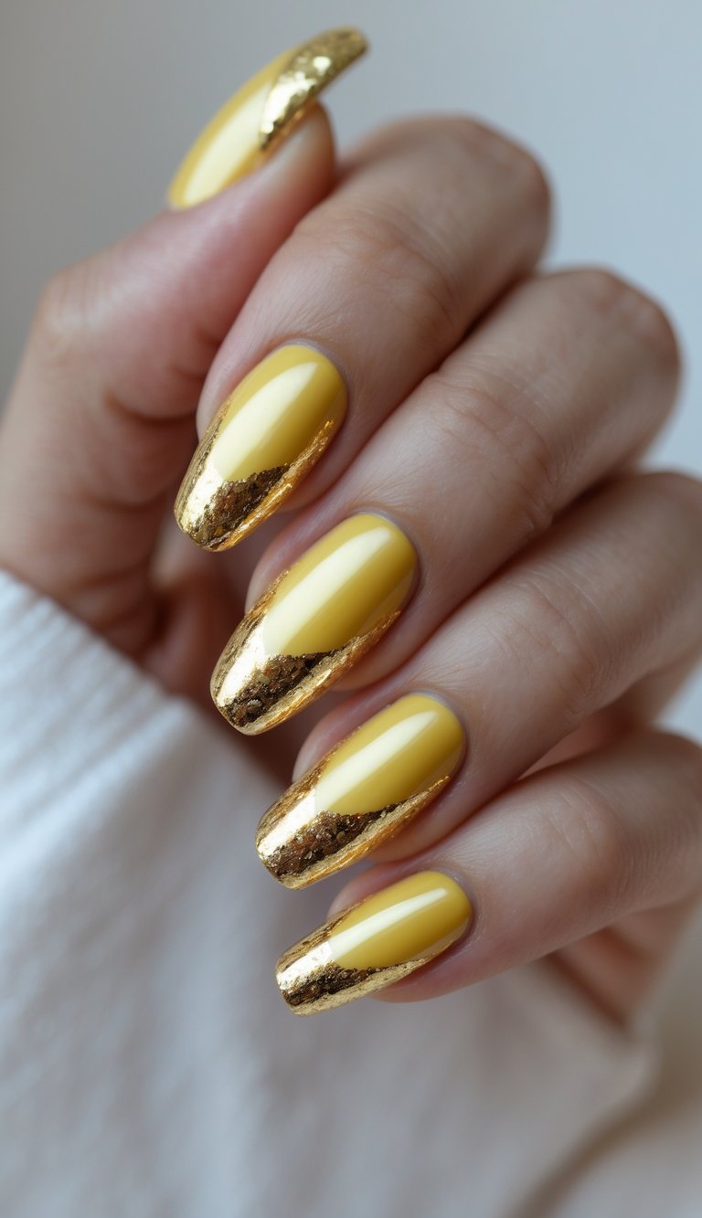 Close-up of one hand with golden yellow nails and gold foil nail art against a white background.