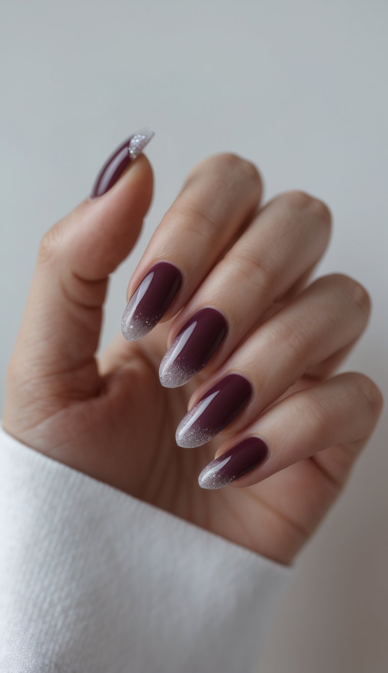 Close-up of one hand with wine-colored nails featuring subtle sparkling tips against a white background.