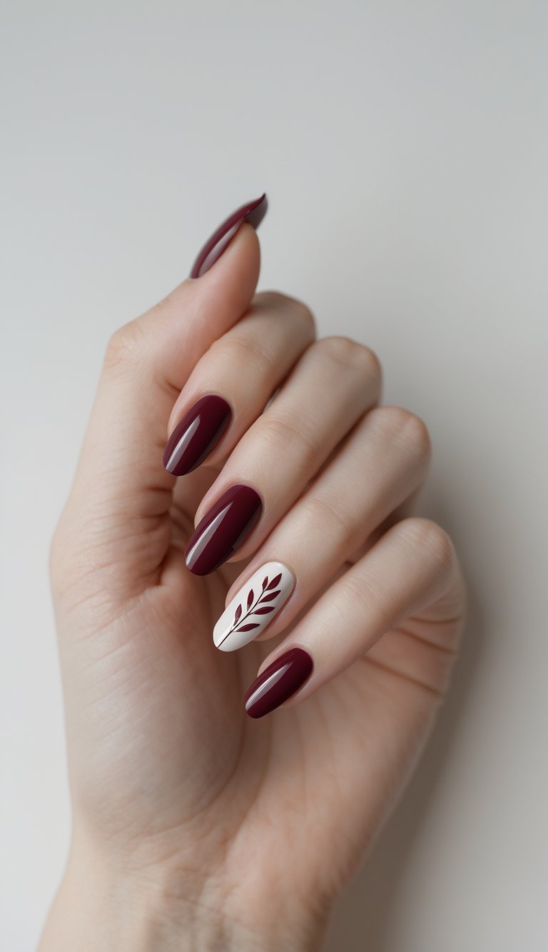 Close-up of one hand with wine red nails and simple leaf nail art against a white background.