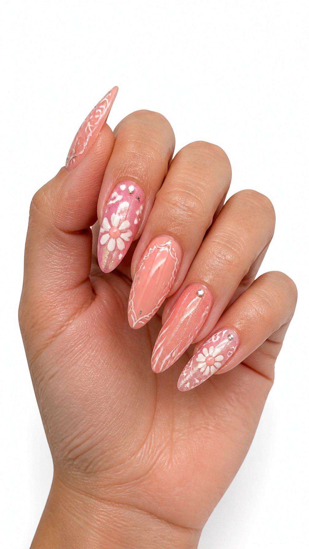 A single hand displays long coral-pink acrylic nails with intricate white designs and small sparkling accents against a white background.