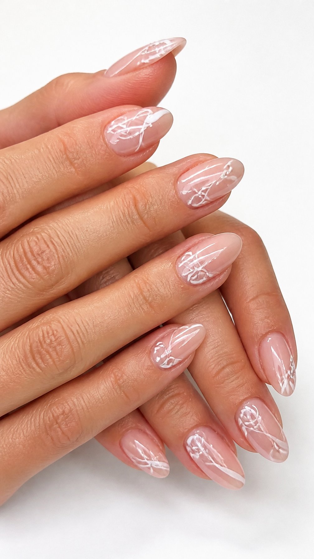A single hand with glossy nude almond-shaped nails decorated with delicate white swirls and small sparkling accents.